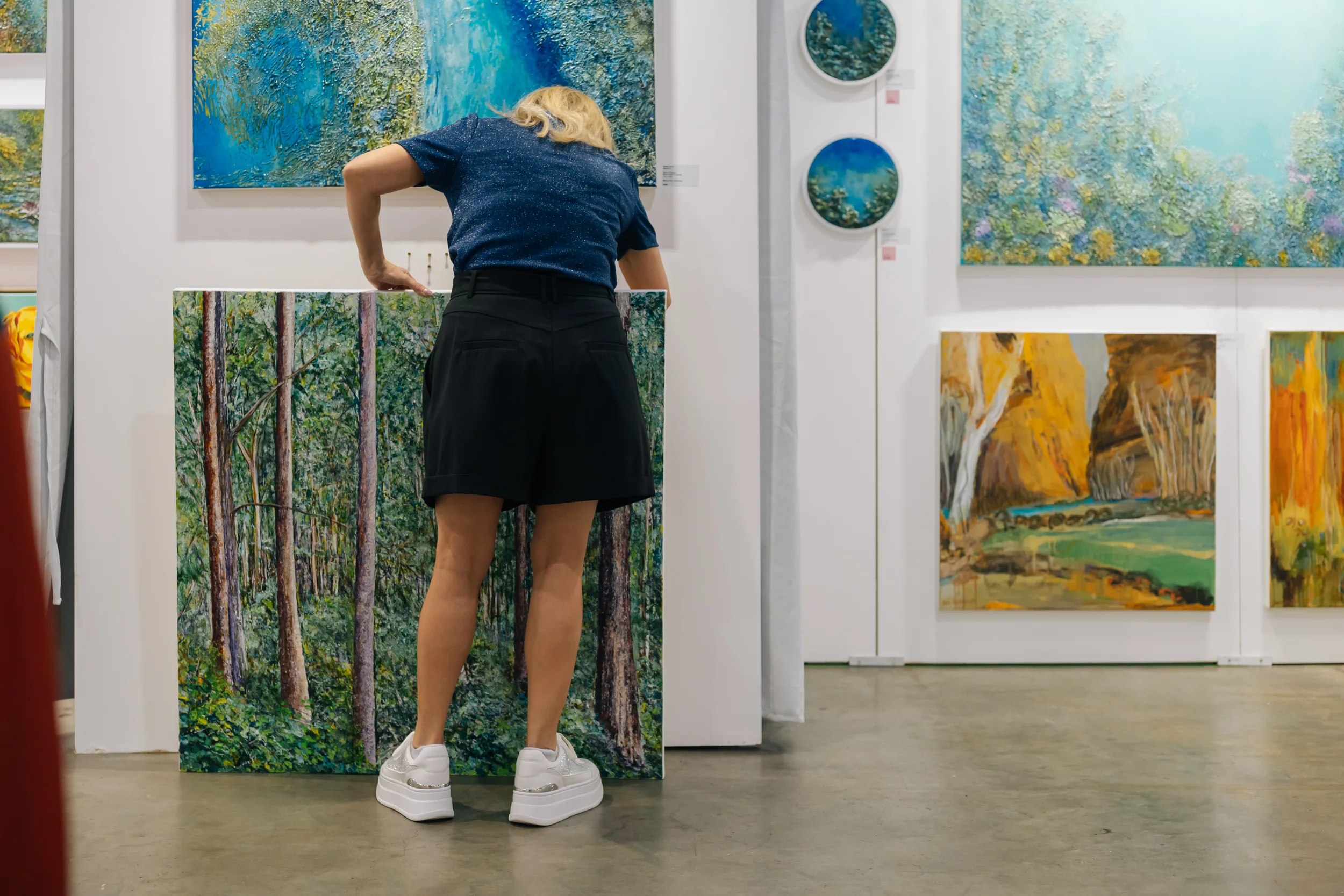 Image of Woman placing landscape painting onto wall 